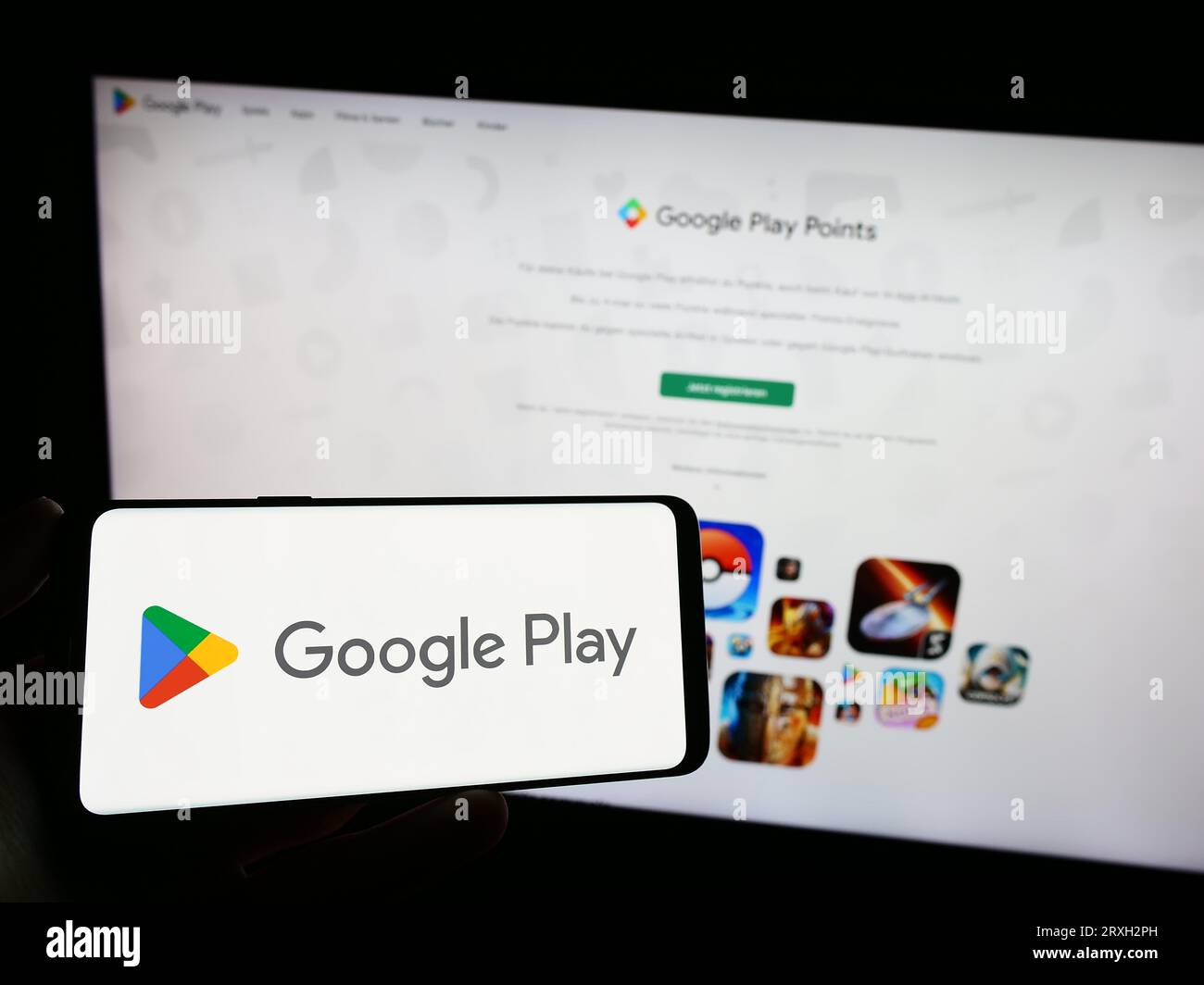 Persona che possiede un telefono cellulare con il logo della piattaforma di distribuzione delle app Google Play sullo schermo davanti alla pagina Web dell'azienda. Concentrarsi sul display del telefono. Foto Stock