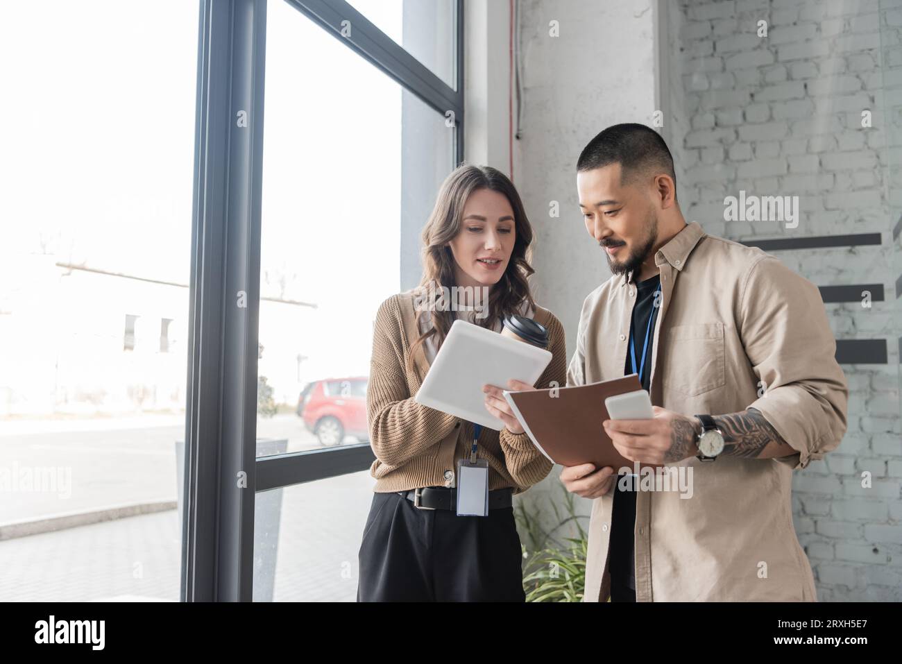 donna d'affari felice che mostra un tablet con progetto di avvio a un collega asiatico in un ufficio moderno Foto Stock