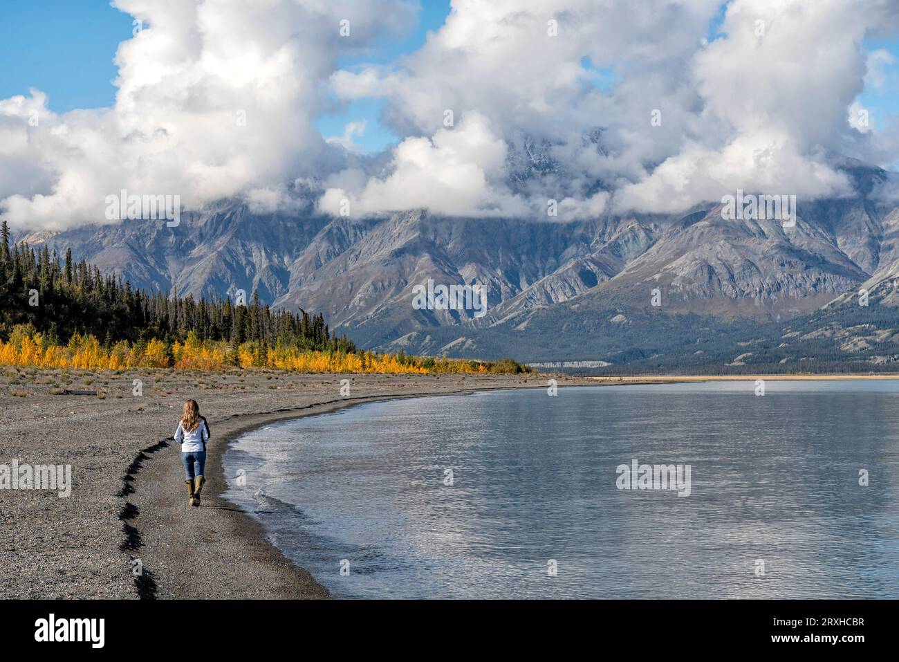 Donna che cammina sulle rive del lago Kluane con montagne intorno a lei. Una scena incredibilmente bella; Yukon, Canada Foto Stock