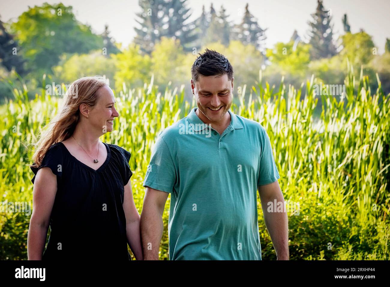 Marito e moglie camminano e si tengono per mano mentre trascorrono del tempo insieme in un parco cittadino durante un caldo pomeriggio autunnale: Leduc, Alberta, Canada Foto Stock