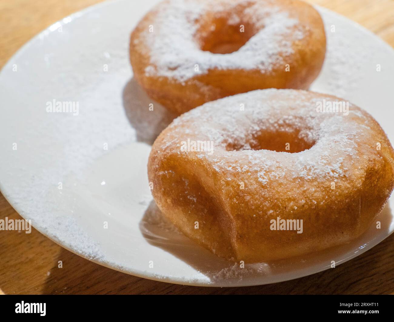Dolci ciambelle gustose cosparse di zucchero a velo sul piatto bianco su sfondo di legno Foto Stock
