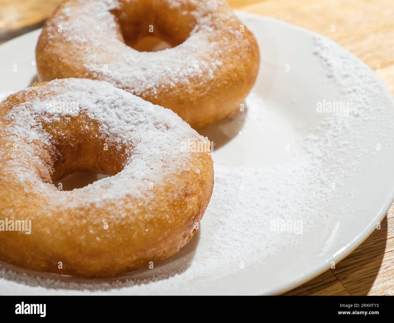 Dolci ciambelle gustose cosparse di zucchero a velo sul piatto bianco su sfondo di legno Foto Stock