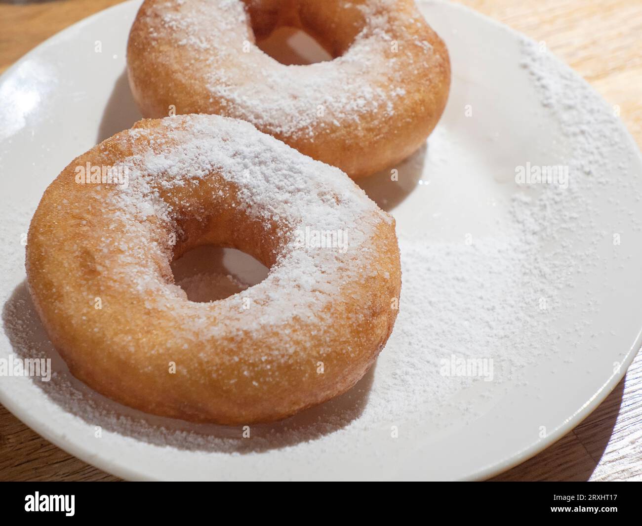 Dolci ciambelle gustose cosparse di zucchero a velo sul piatto bianco su sfondo di legno Foto Stock