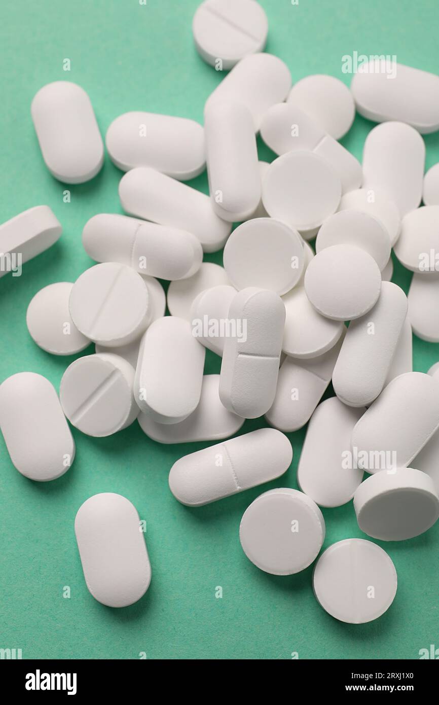 Pila di pillole bianche su sfondo verde, posato piatto Foto Stock