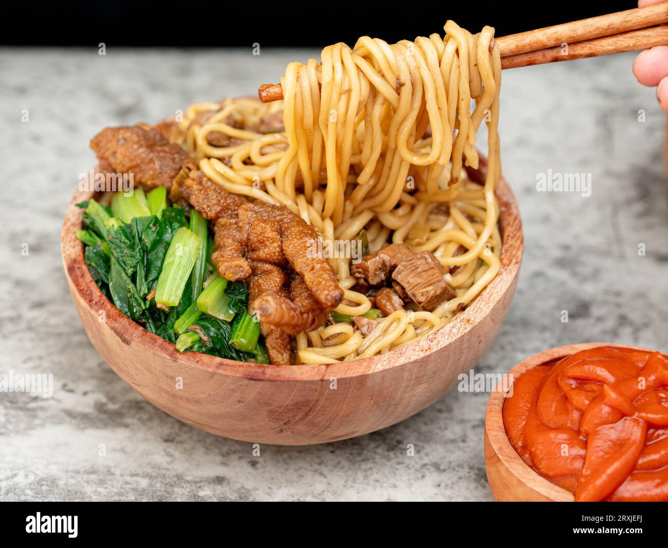Spaghetti di pollo indonesiani chiamati mie ayam conditi con carne di pollo e senape verde serviti in una ciotola con salsa rossa speziata Foto Stock