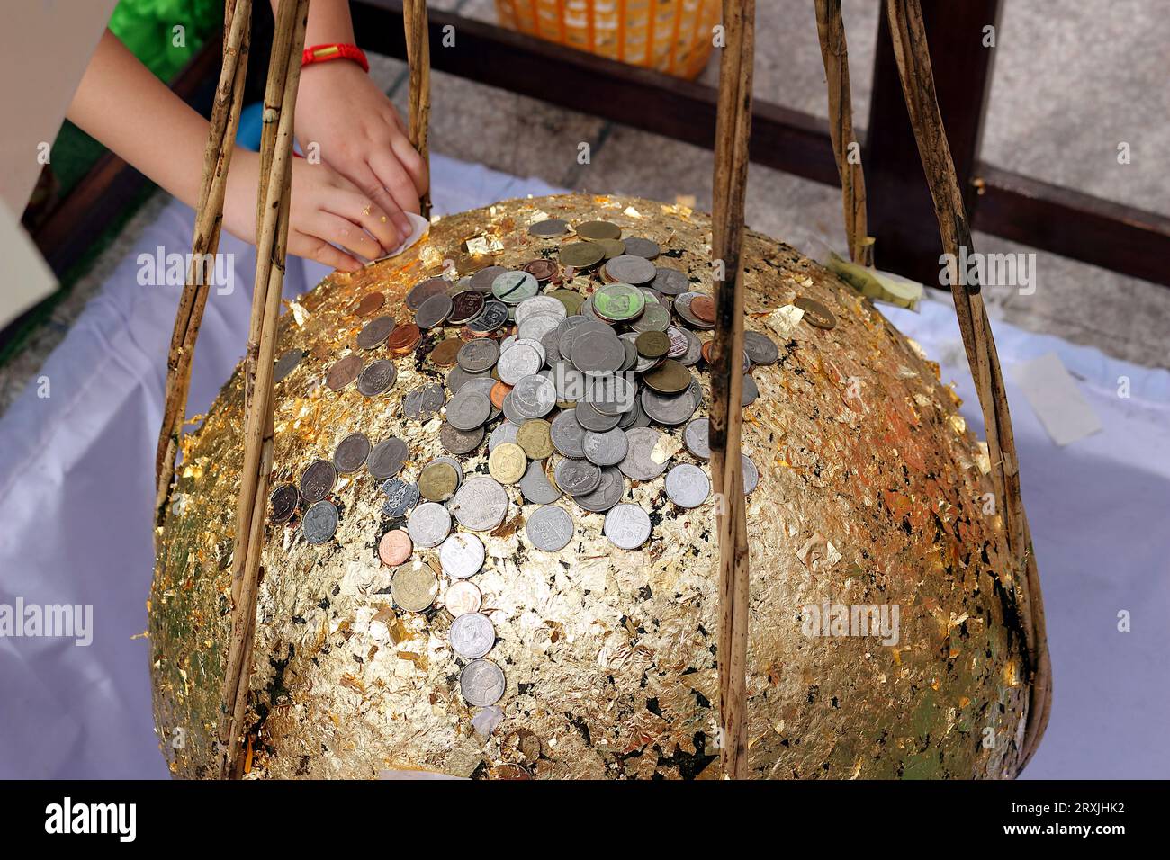 Una foto di uno stupa dorato da bambini e anziani, con lo stupa ricoperto di foglia d'oro e molte monete d'argento poste su di esso. Foto Stock