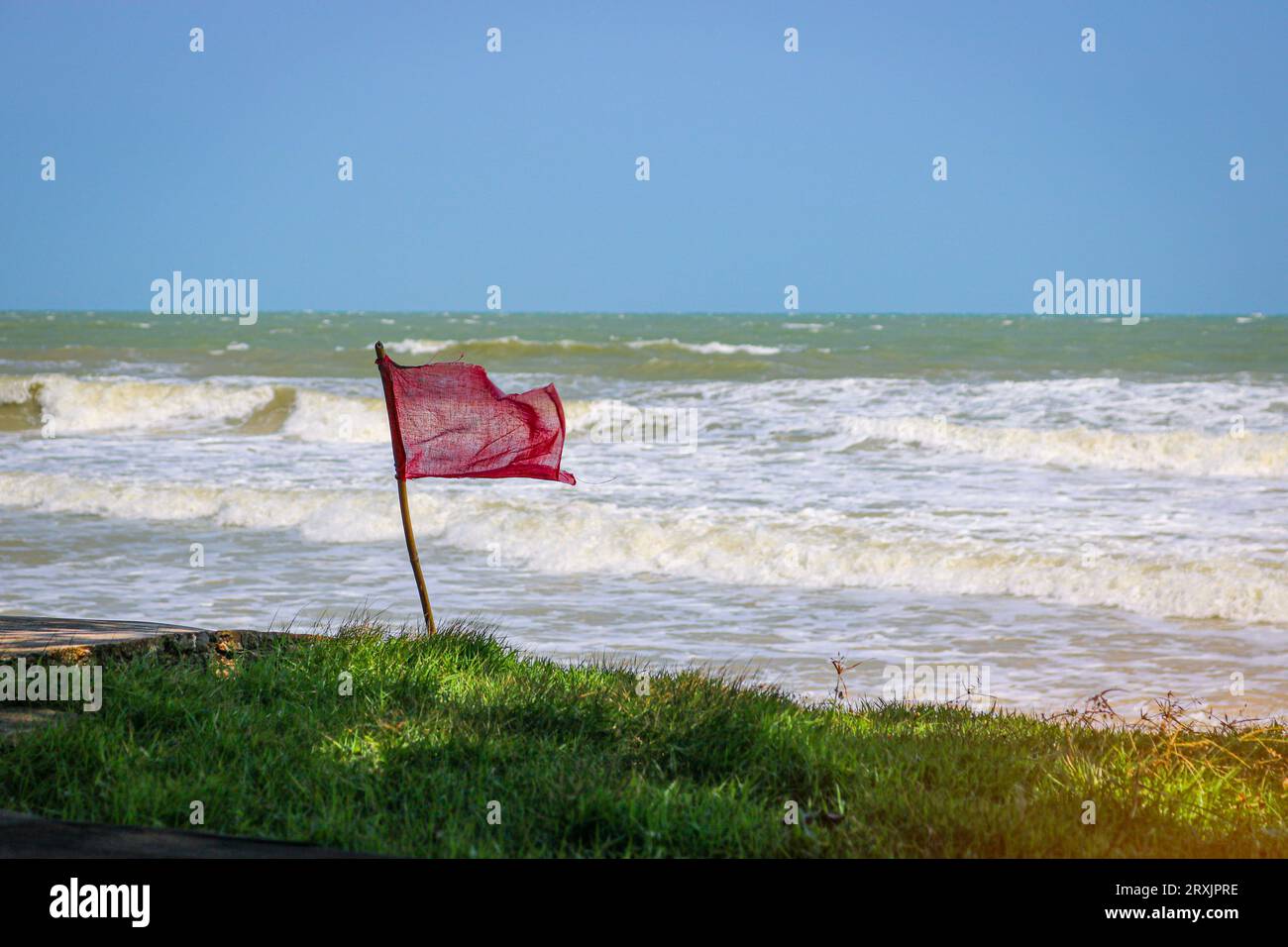 Bandiera rossa che sbatte nel vento sulla spiaggia durante il tempo tempestoso. Nuotare è pericoloso nelle onde marine. Foto Stock
