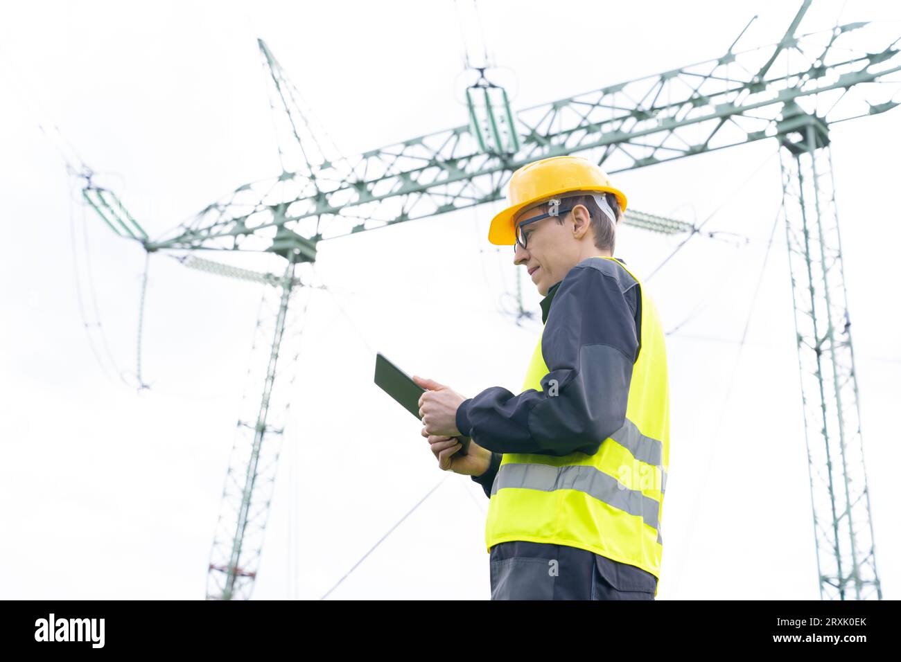Progettare con un tablet digitale sullo sfondo di una torre della linea elettrica. Foto Stock