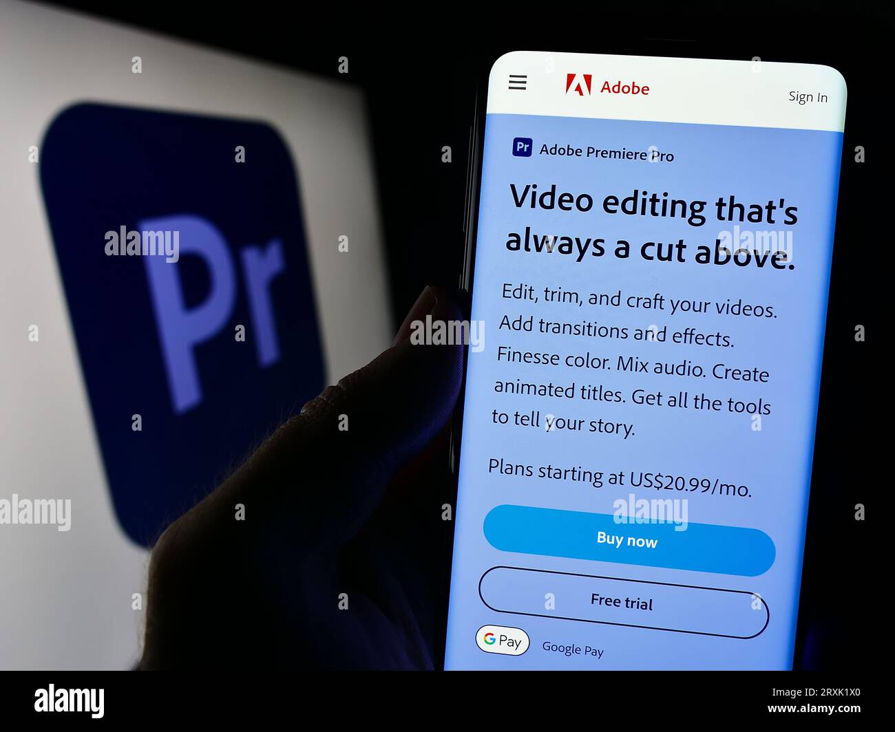 Persona che possiede il cellulare con una pagina Web del software di editing video Adobe Premiere Pro sullo schermo davanti al logo. Concentrarsi sul centro del display del telefono. Foto Stock