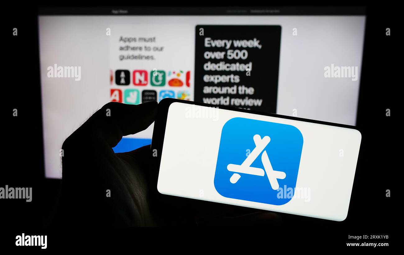 Persona che possiede il cellulare con il logo della piattaforma di mercato Apple App Store sullo schermo di fronte alla pagina Web aziendale. Concentrarsi sul display del telefono. Foto Stock