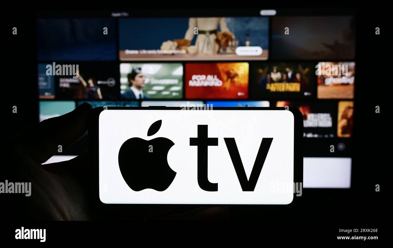 Persona che possiede uno smartphone con il logo del servizio di streaming video Apple TV Plus sullo schermo davanti al sito Web. Concentrarsi sul display del telefono. Foto Stock