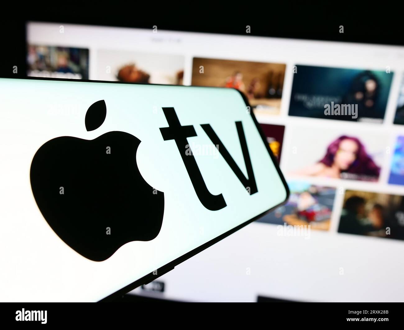 Smartphone con logo del servizio di streaming video Apple TV Plus sullo schermo di fronte al sito Web aziendale. Mettere a fuoco il display centrale sinistro del telefono. Foto Stock