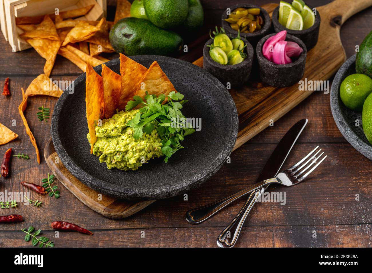 Guacamole all'avocado con tortillas croccanti su un piatto di pietra nera su un tavolo di legno Foto Stock