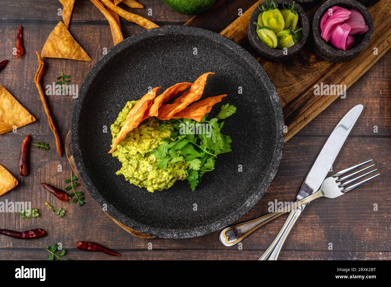 Guacamole all'avocado con tortillas croccanti su un piatto di pietra nera su un tavolo di legno Foto Stock