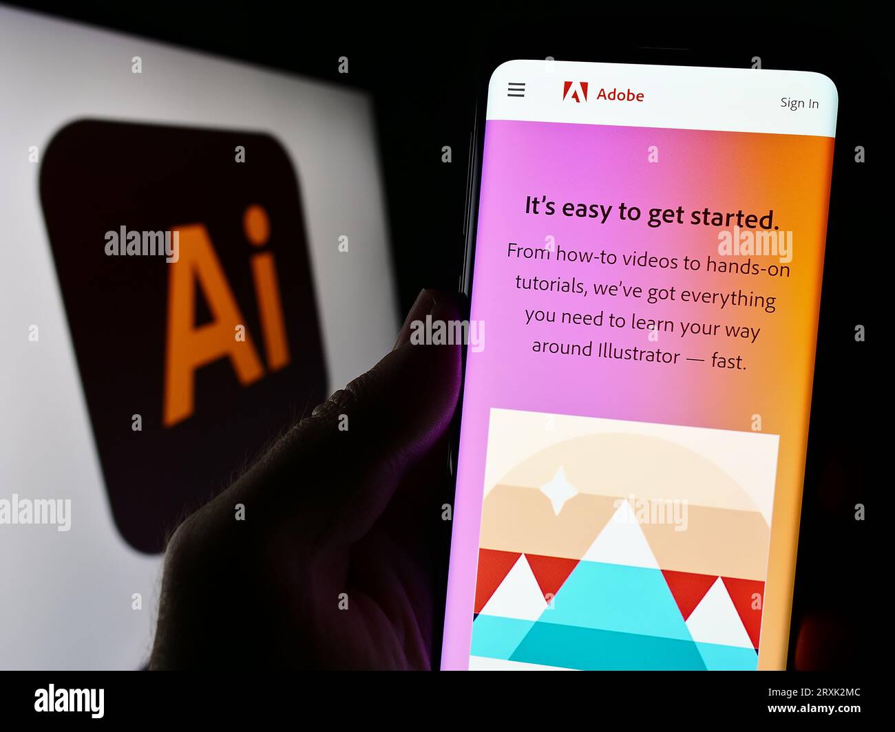 Persona che possiede il cellulare con una pagina Web dell'editor di grafica vettoriale Adobe Illustrator sullo schermo davanti al logo. Concentrarsi sul centro del display del telefono. Foto Stock