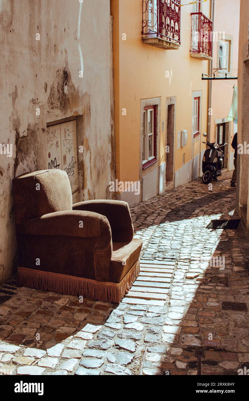 Vecchia poltrona abbandonata su Lisbona Street, Portogallo. Poltrona marrone rétro all'esterno dell'edificio. Mobili rotti vintage. Strada stretta con mobili retrò Foto Stock