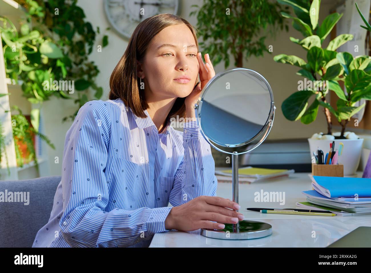 Giovane donna attraente con trucco naturale che guarda allo specchio Foto Stock
