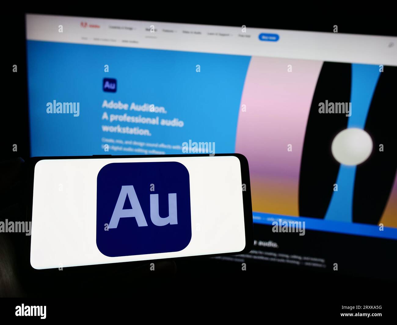Persona che possiede un telefono cellulare con il logo della workstation audio digitale Adobe Audition sullo schermo davanti alla pagina Web dell'azienda. Concentrarsi sul display del telefono. Foto Stock