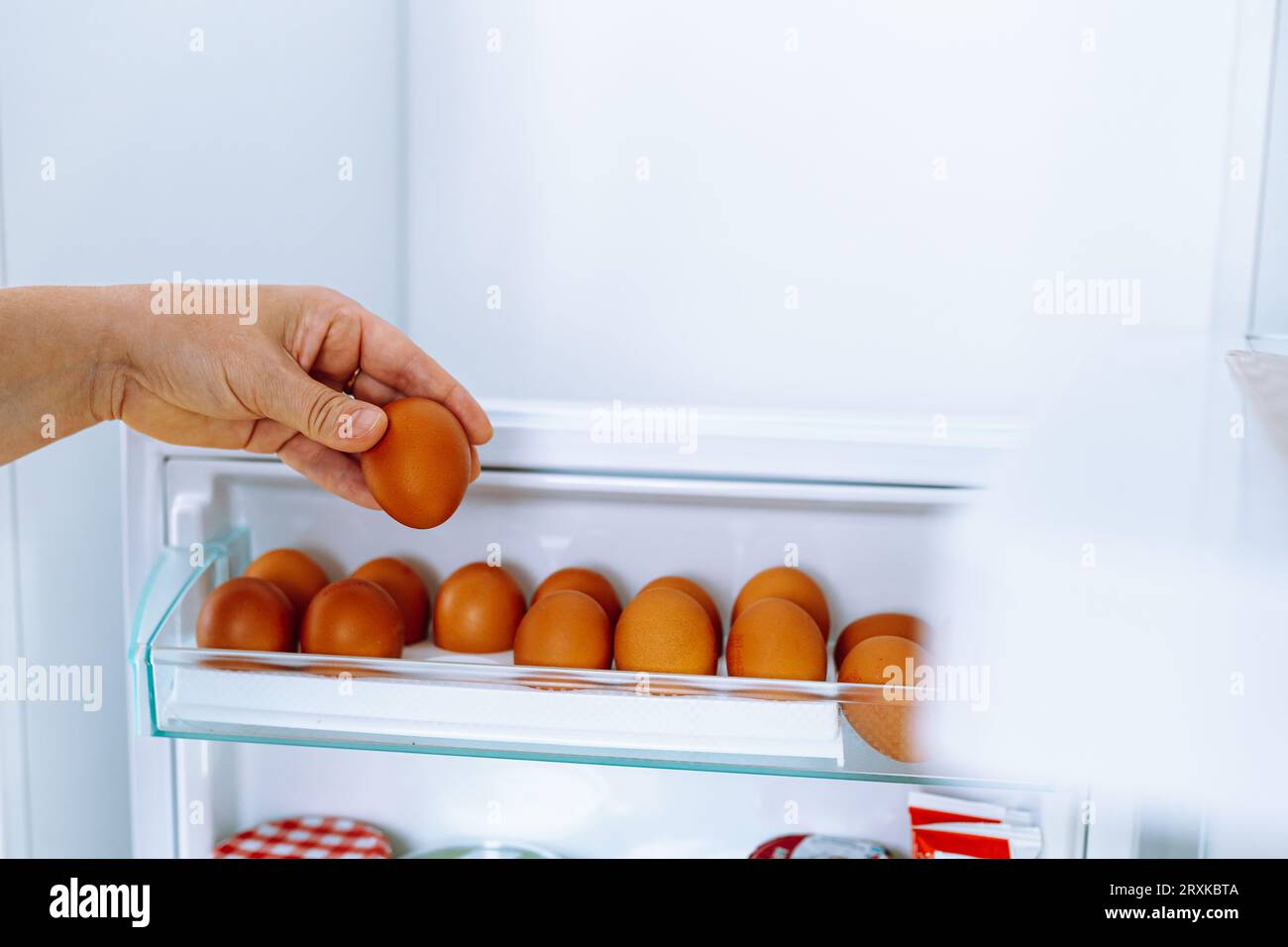 Chiudi le mani umane metti le uova di gallina nel vano per la deposizione delle uova in frigorifero Foto Stock