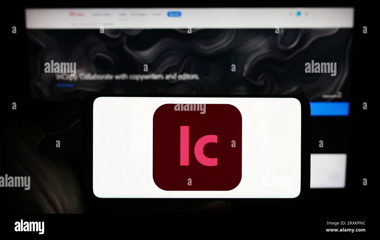 Persona che possiede il cellulare con il logo del software di elaborazione testi Adobe InCopy sullo schermo davanti alla pagina Web aziendale. Concentrarsi sul display del telefono. Foto Stock