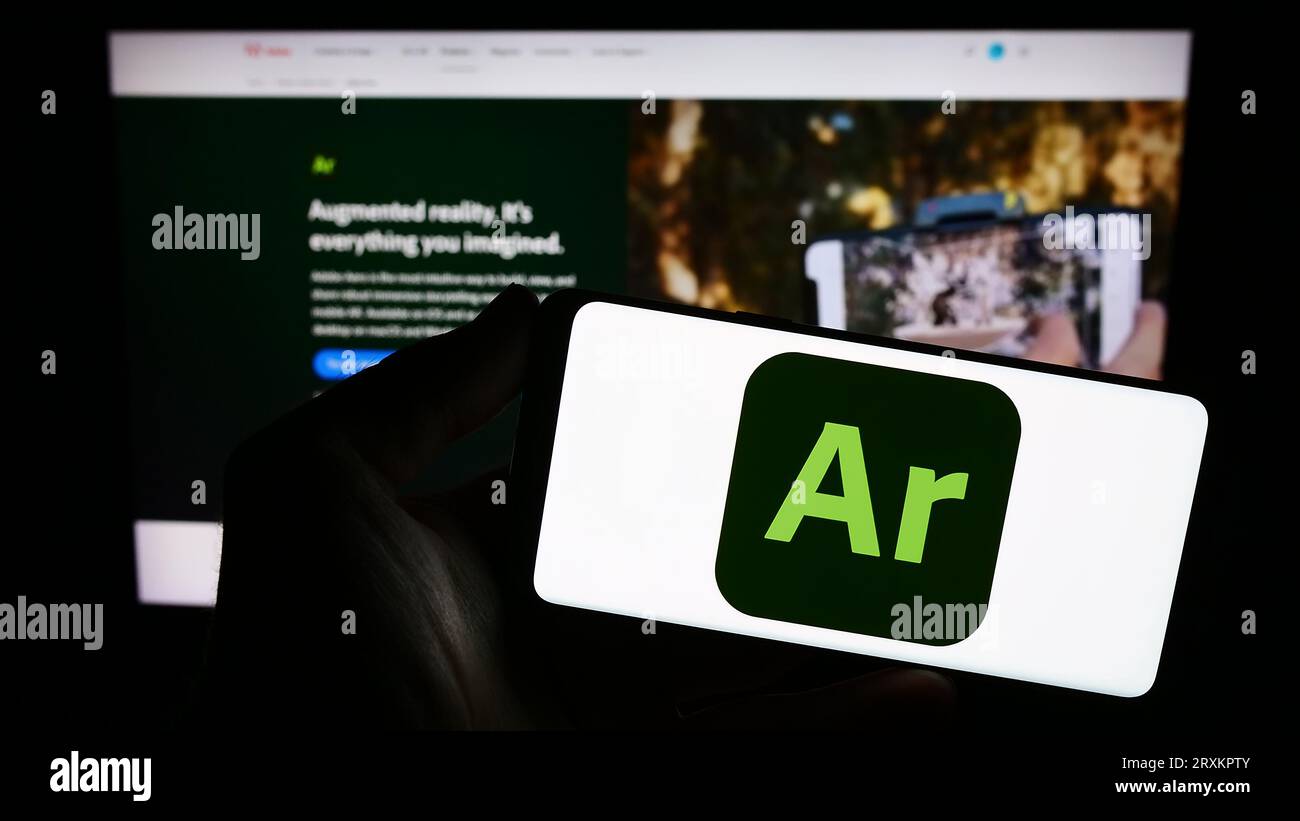 Persona che possiede uno smartphone con il logo del software di realtà aumentata Adobe Aero sullo schermo davanti al sito Web. Concentrarsi sul display del telefono. Foto Stock