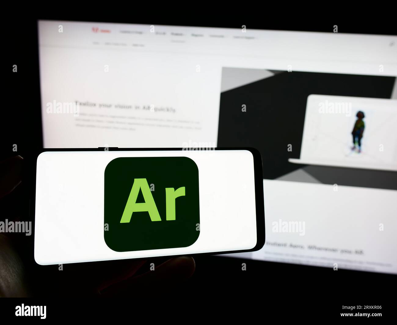 Persona che possiede il cellulare con il logo del software di realtà aumentata Adobe Aero sullo schermo davanti alla pagina Web aziendale. Concentrarsi sul display del telefono. Foto Stock