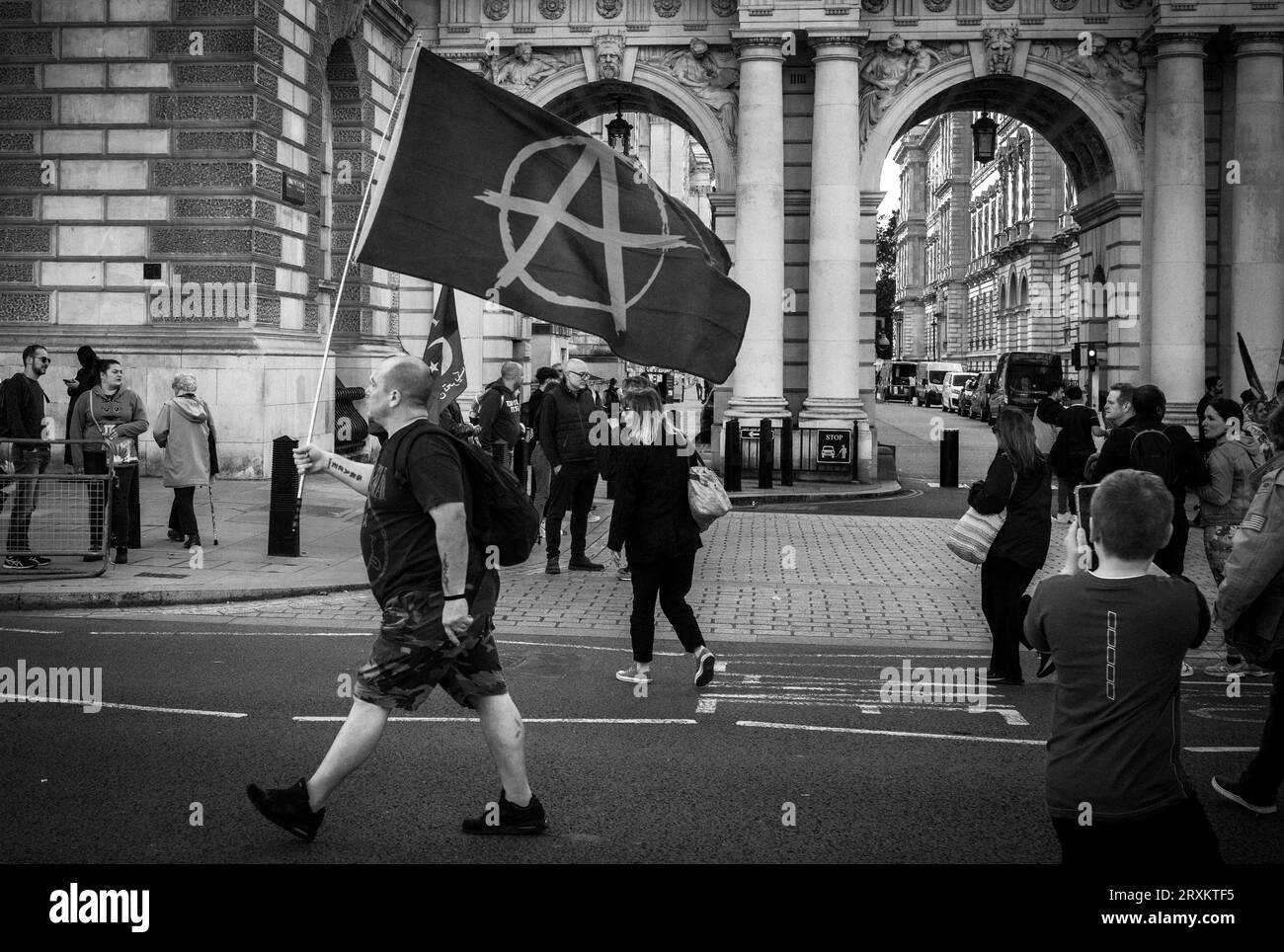 Un uomo porta una bandiera anarchica davanti al Ministero degli Esteri del governo britannico e ai turisti mentre cammina lungo Whitehall nel centro di Londra. Era stato atte Foto Stock