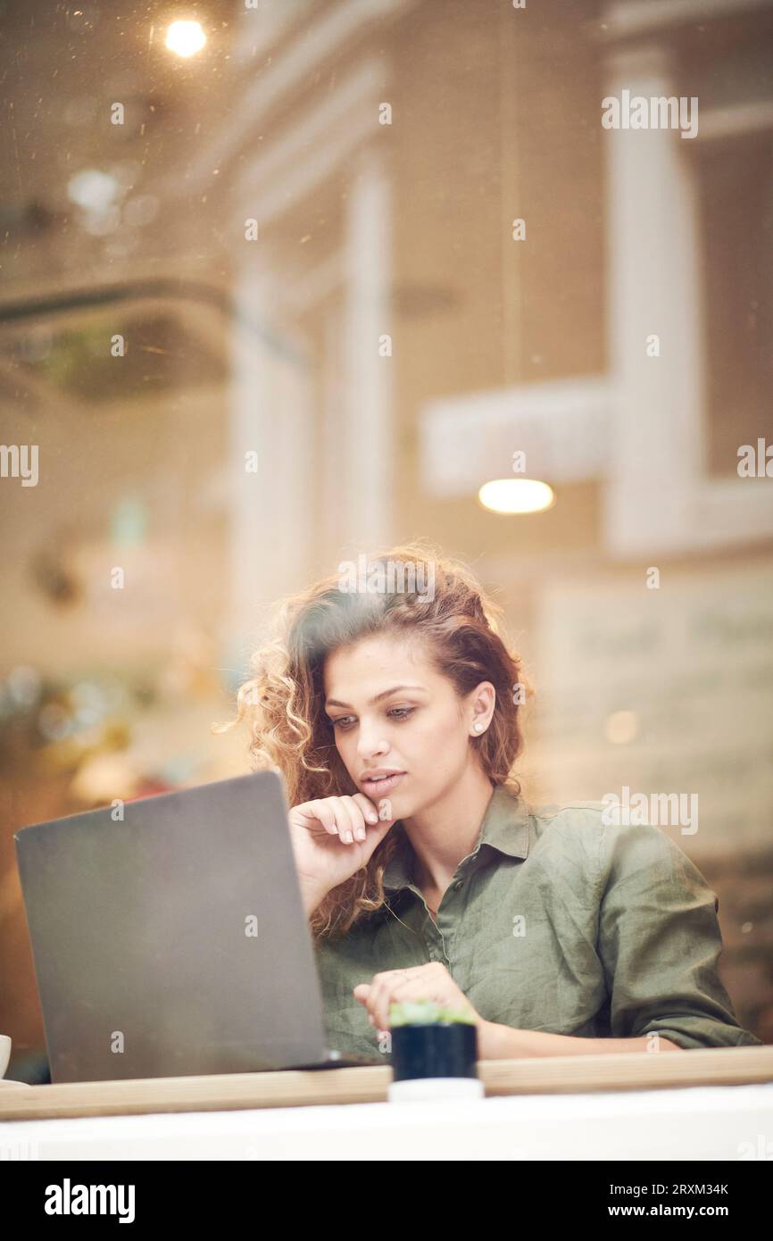 Giovane donna utilizzando laptop dietro la finestra cafe Foto Stock