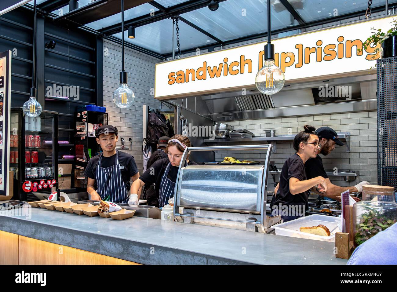 Persone che preparano cibo in uno dei molti punti vendita di cibo all'Old Spitalfields Market, Londra E1 Foto Stock
