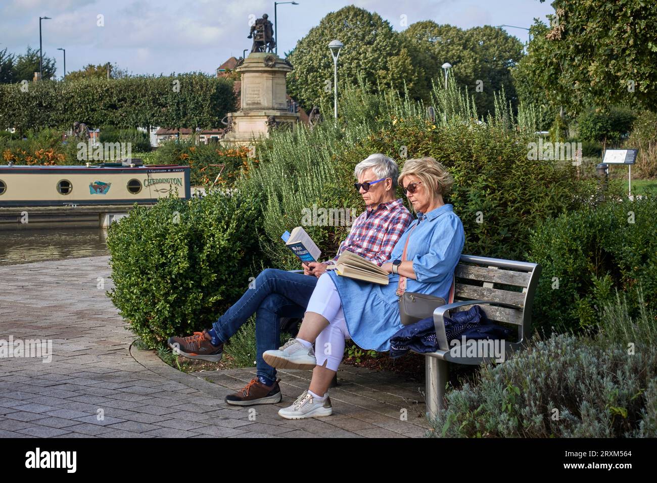 Coppia che leggeva un libro all'aperto seduto su una panchina a Stratford Upon Avon, Warwickshire, Inghilterra Regno Unito. Insieme, come persone di mentalità Foto Stock