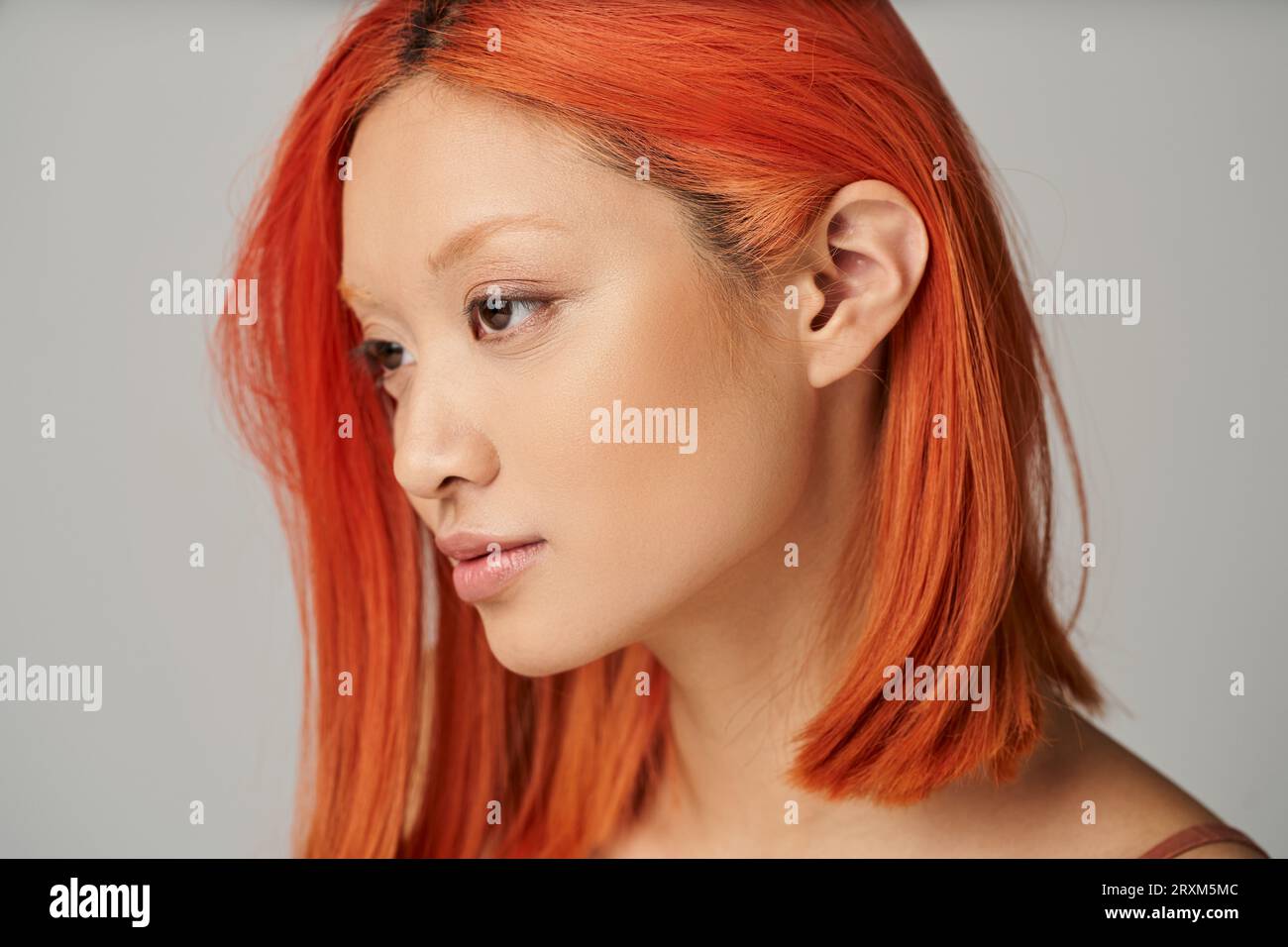 ritratto di una giovane donna asiatica delicata con pelle perfetta e capelli rossi in posa su sfondo grigio Foto Stock