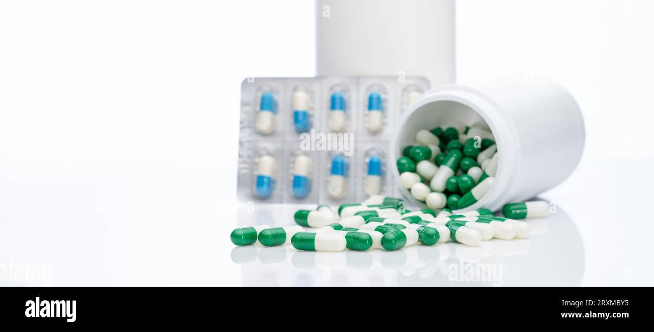 Pillole di capsule verdi-bianche su blister sfocato confezione di pillole di capsule blu-bianche e flacone di droga. Le pillole fuoriescono dal flacone di plastica. Farmaceutico Foto Stock