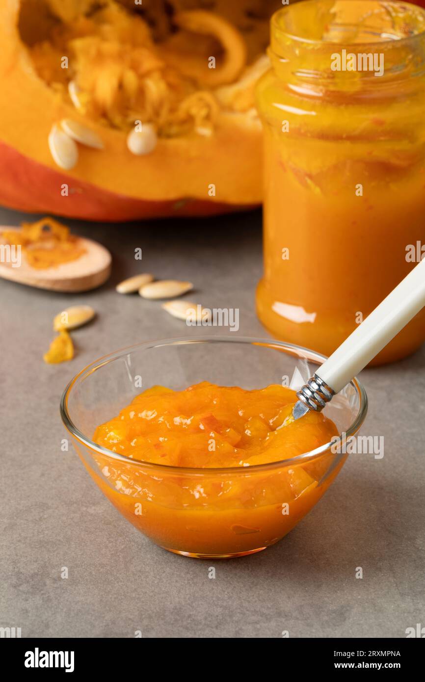 Ciotola di vetro con marmellata di zucca arancione fatta in casa da vicino davanti a una zucca fresca Foto Stock