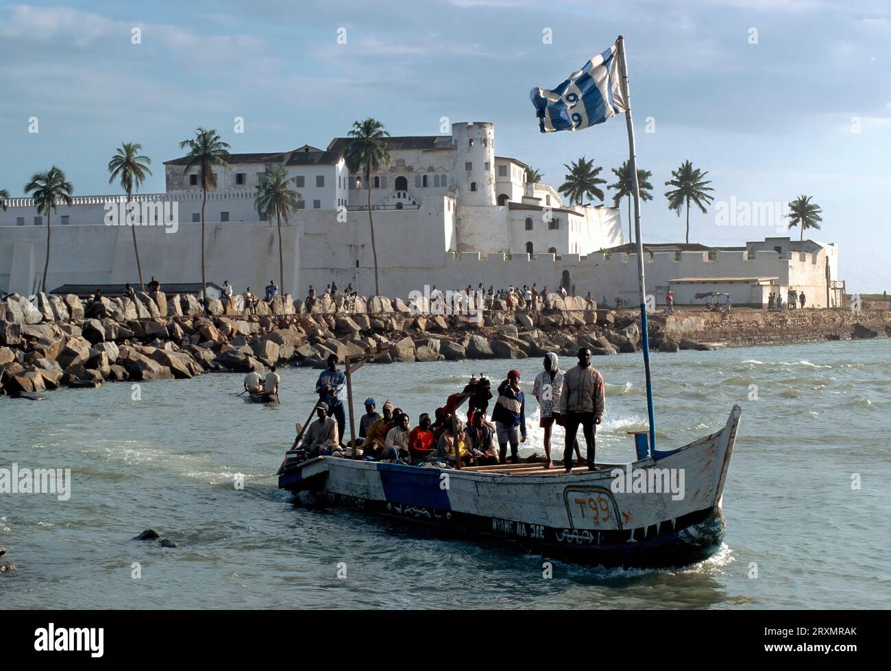 GHA, Ghana: Barca di fronte a Fort Elmina. Costruito dai portoghesi nel XV secolo e successivamente di proprietà degli olandesi e degli inglesi, Fort Elmina deteneva gli africani prima della spedizione verso i mercati degli schiavi delle Americhe Foto Stock
