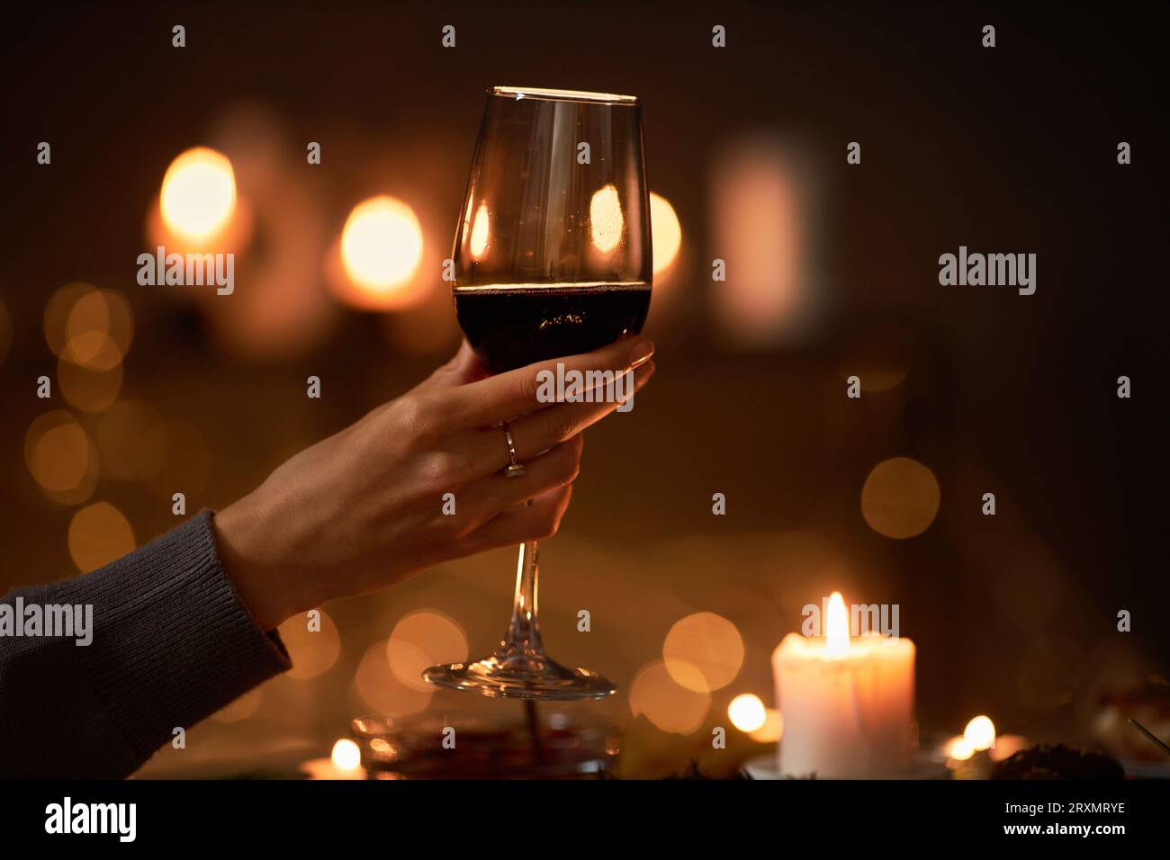 Primo piano della mano femminile che tiene un bicchiere di vino al tavolo della cena con luci di Natale sullo sfondo, spazio per le copie Foto Stock