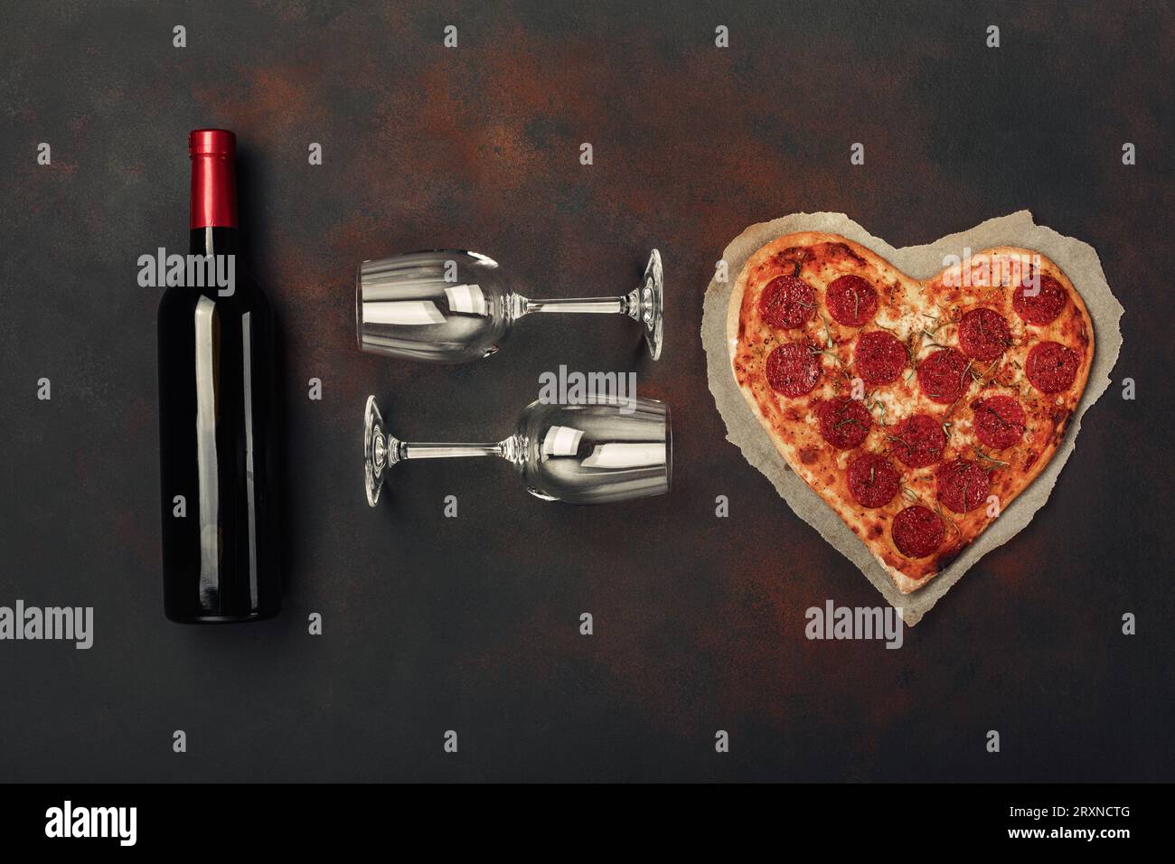 Pizza a forma di cuore con mozzarella, salsiccia, bottiglia di vino e due bicchieri di vino. Biglietto d'auguri per San Valentino. Vista dall'alto Foto Stock