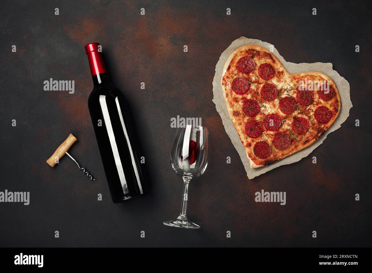 Pizza a forma di cuore con mozzarella, salsiccia e bottiglia di vino, vetro e cavatappi. Biglietto d'auguri di San Valentino su sfondo arrugginito. Vista dall'alto Foto Stock