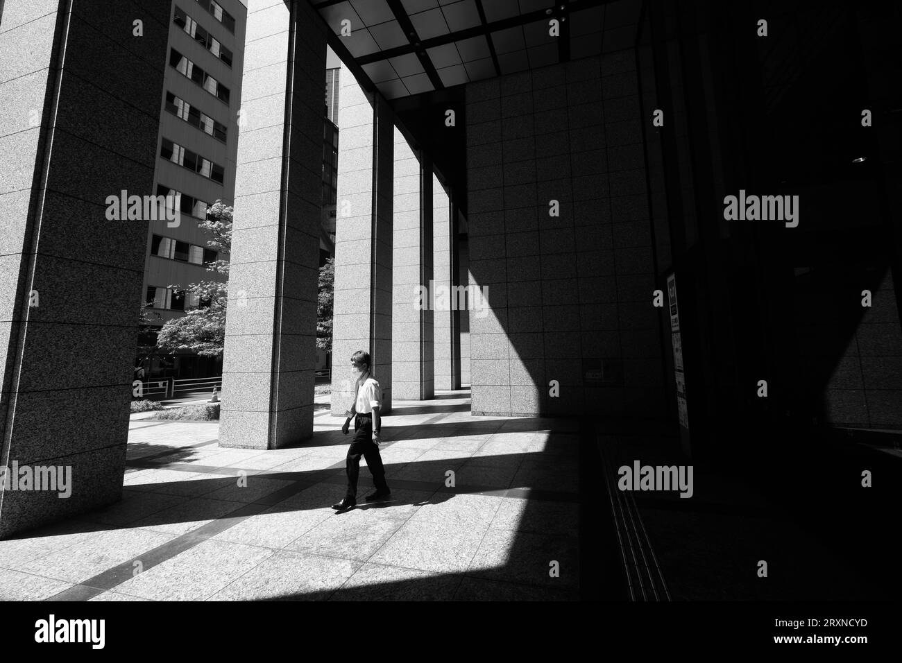 Un uomo illuminato dal sole cammina tra le ombre di un complesso di uffici a Nihonbashi, Tokyo, Giappone Foto Stock