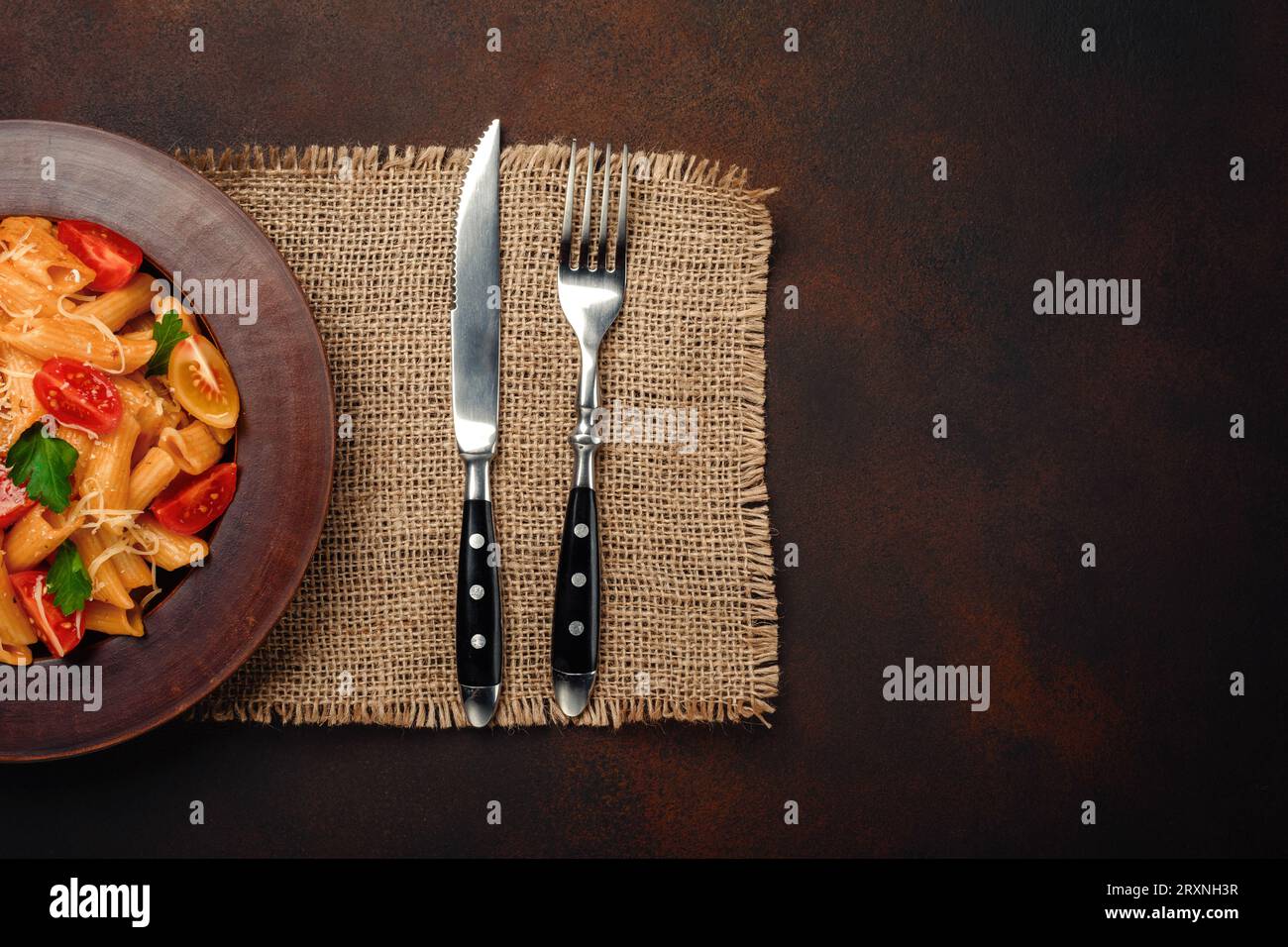 Pasta con formaggio, pomodoro ciliegia, forchetta e coltello su fondo arrugginito, vista dall'alto. Foto Stock
