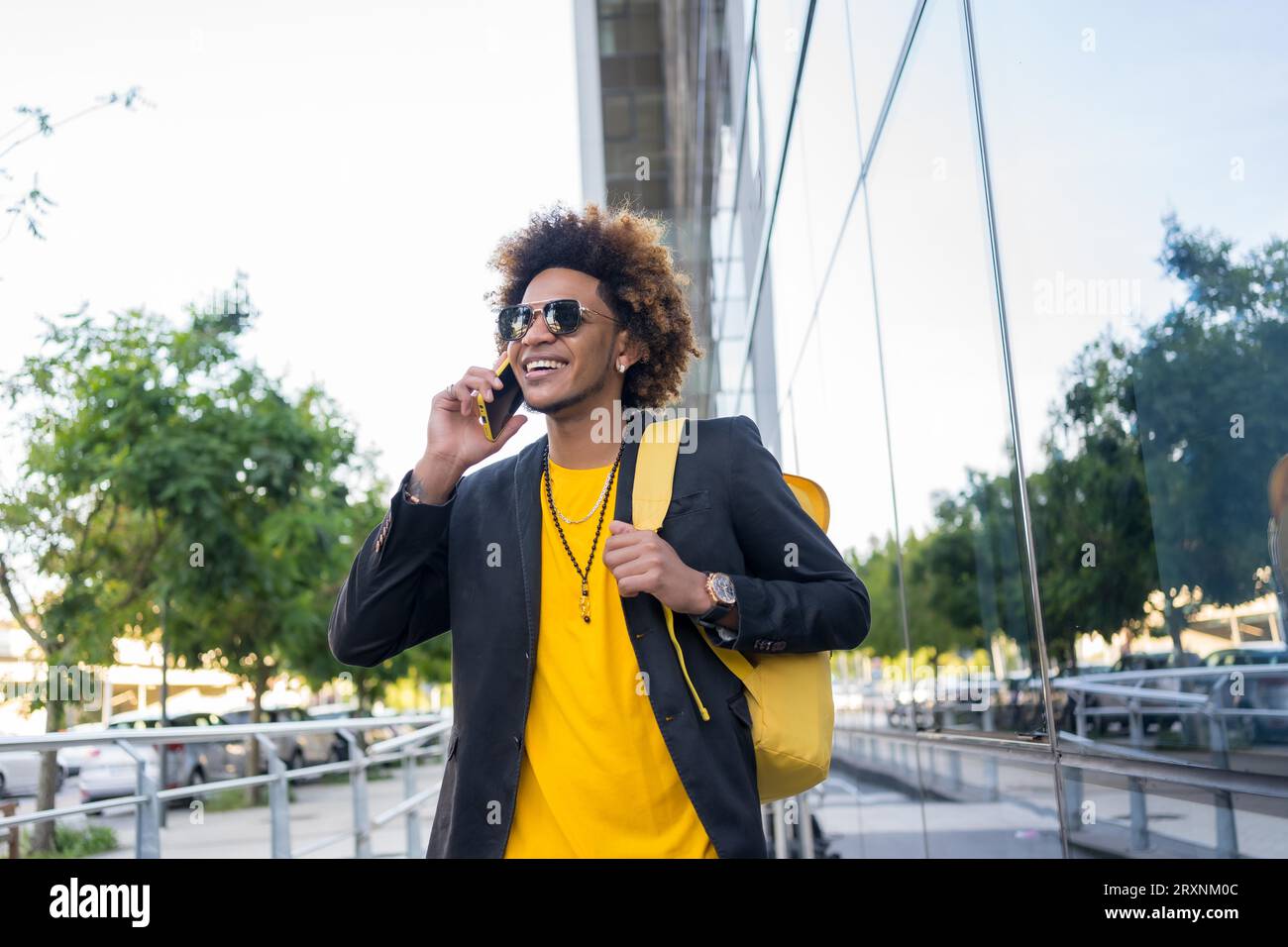 Uomo afro-americano casual ed elegante che parla al telefono mentre è in viaggio con una borsa Foto Stock