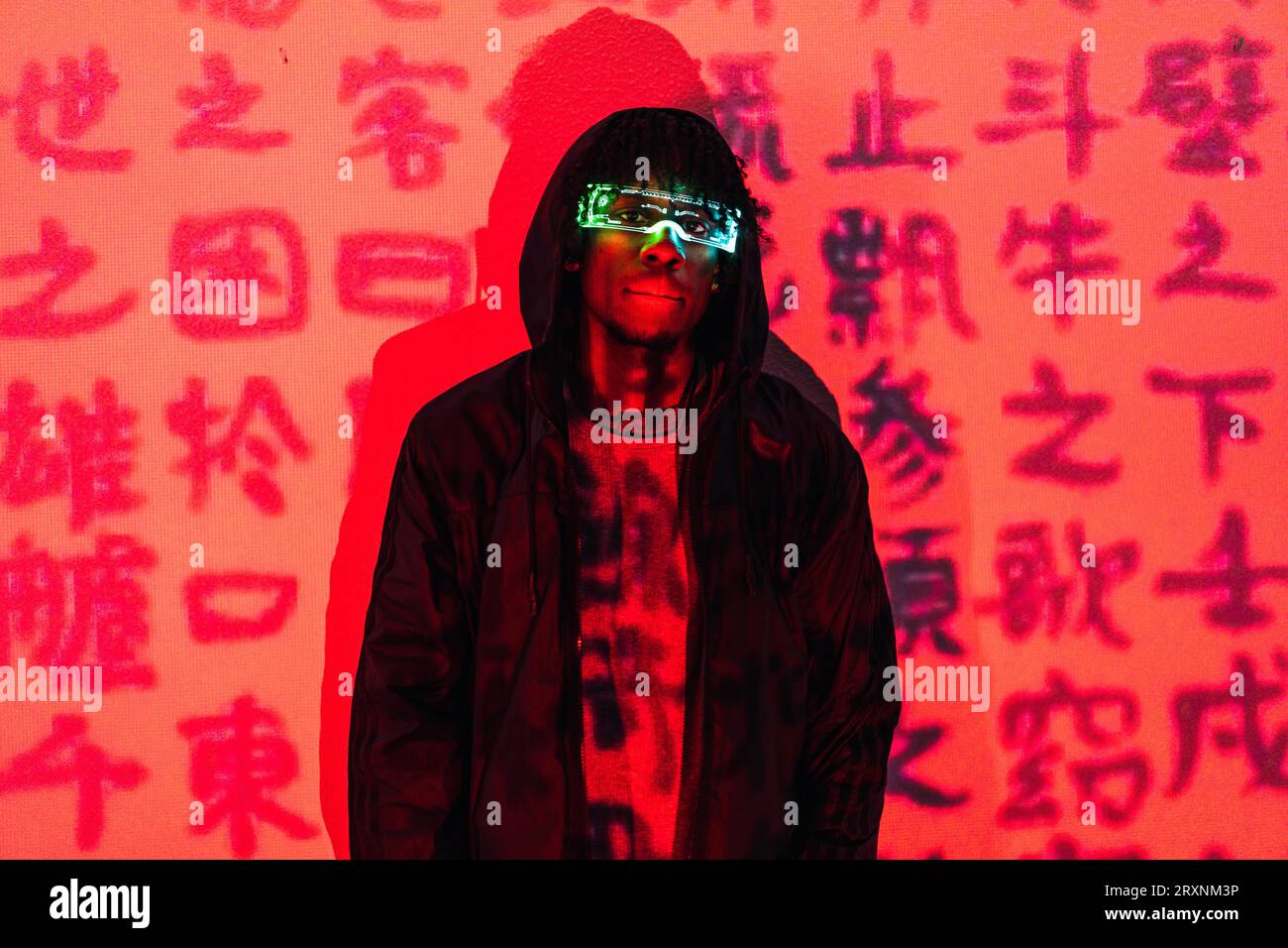 Ritratto in studio con luci al neon rosse di un uomo futuristico con occhiali a maschera in un muro con parole cinesi Foto Stock