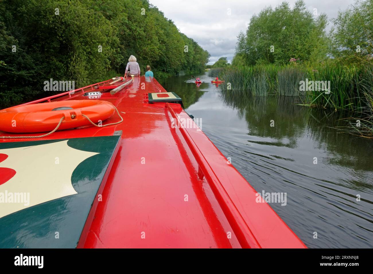 Persone su narrowboatd rossi che guardano i paddleboarder sul tranquillo tratto del fiume Avon vicino a Evesham nel Regno Unito Foto Stock