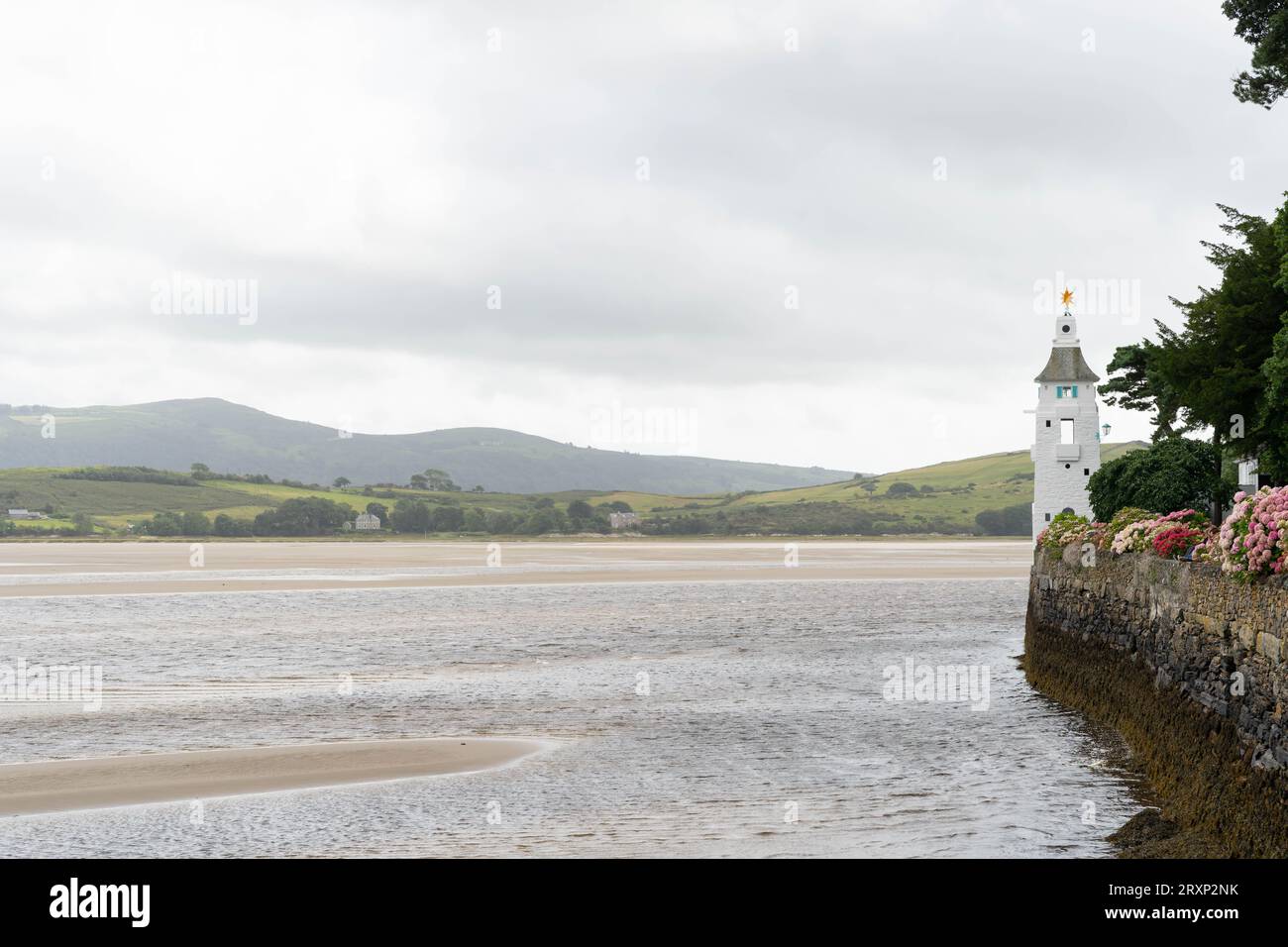 Iconico faro bianco che si affaccia sulle acque dell'estuario con colline gallesi sullo sfondo a Portmeirion Foto Stock