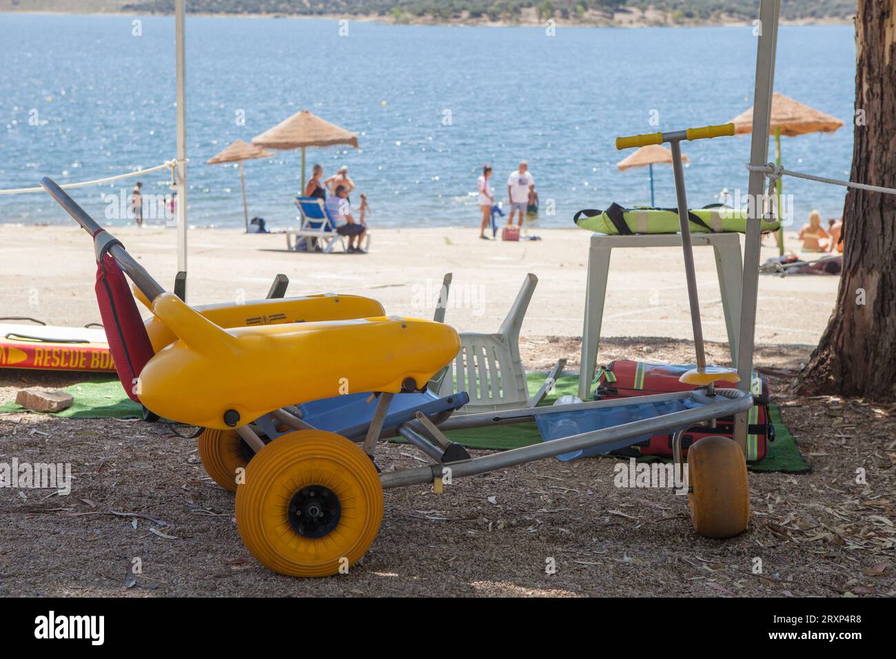 Sedia a rotelle da spiaggia vicino alla riva del lago artificiale pronta per l'uso. Concetto di turismo accessibile con sedia a rotelle Foto Stock Sedia a rotelle da spiaggia vicino alla riva del lago artificiale pronta per l'uso. Concetto di turismo accessibile con sedia a rotelle Foto Stock