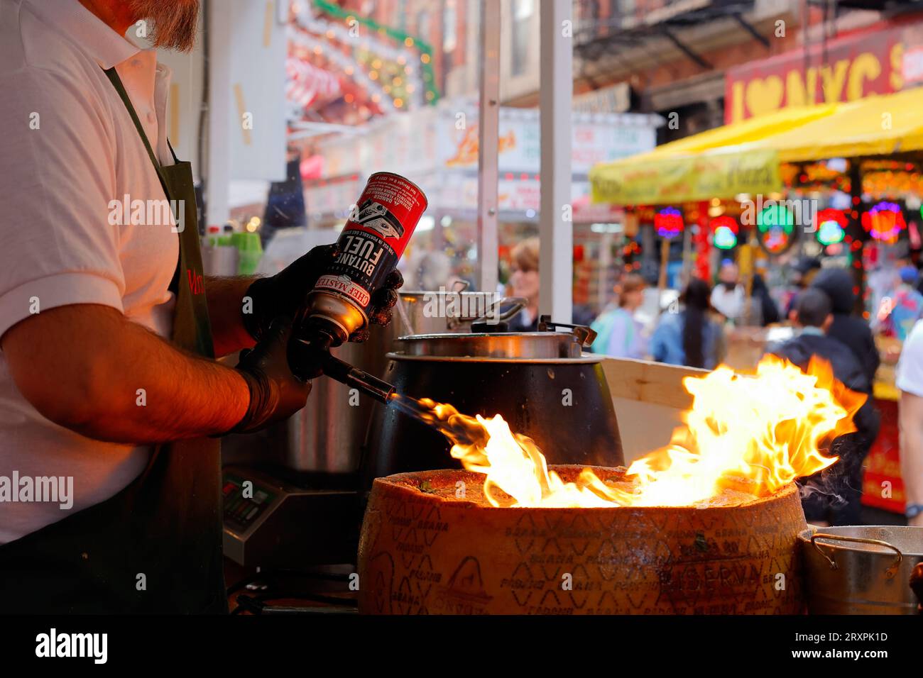 Una chef del Mrs Claus Cafe fonde una ruota di Grana Padano con una torcia per preparare la pasta al formaggio, al San Gennaro Feast, New York City. Foto Stock