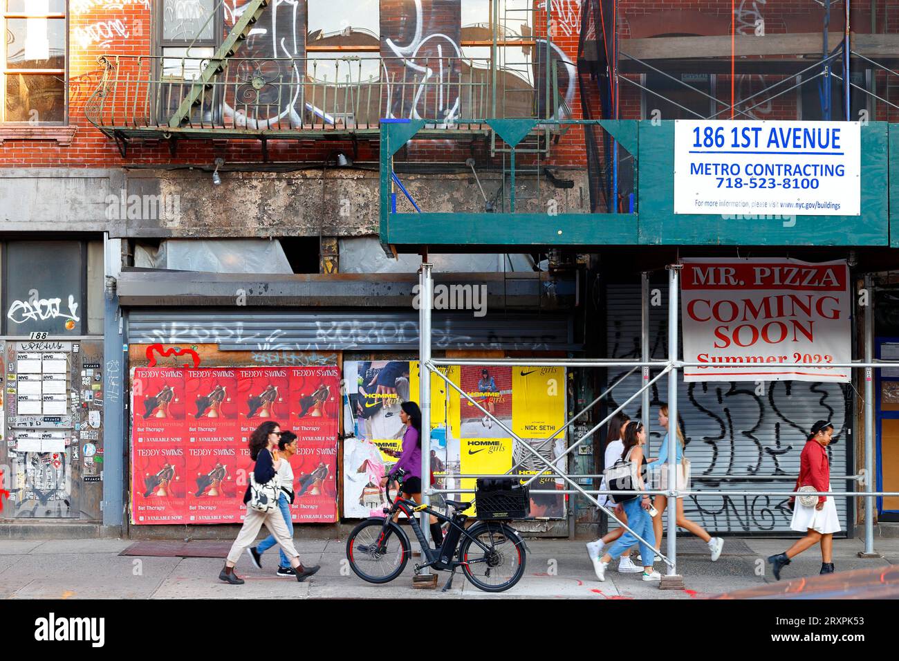 Donne, persone che camminano davanti a edifici con graffiti in fase di ristrutturazione e una pizzeria in costruzione nell'East Village di Manhattan, New York City. Foto Stock