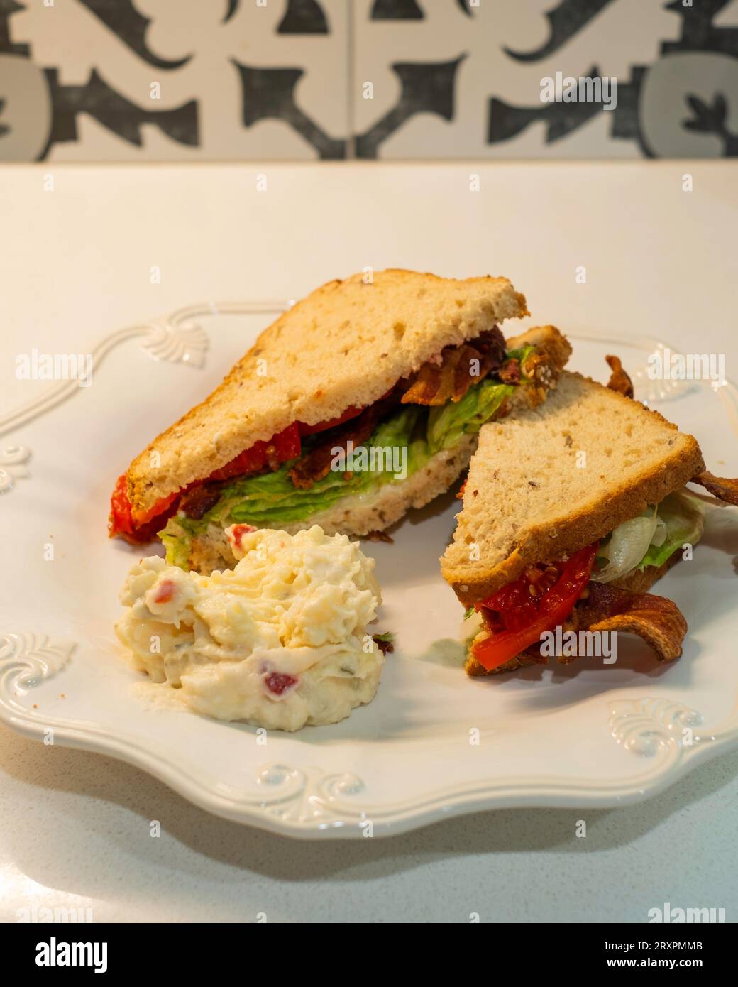 BLT, panino con pancetta, pomodoro e lattuga, con pane di arachidi e una porzione di insalata di patate su un piatto bianco. USA. Foto Stock