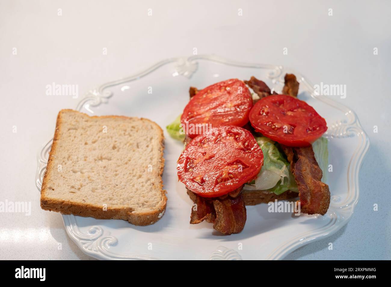 BLT, panino con pancetta, pomodoro e lattuga, preparato con pane di arachidi, con una fetta di pane rimossa che mostra il contenuto, su un piatto bianco. USA. Foto Stock