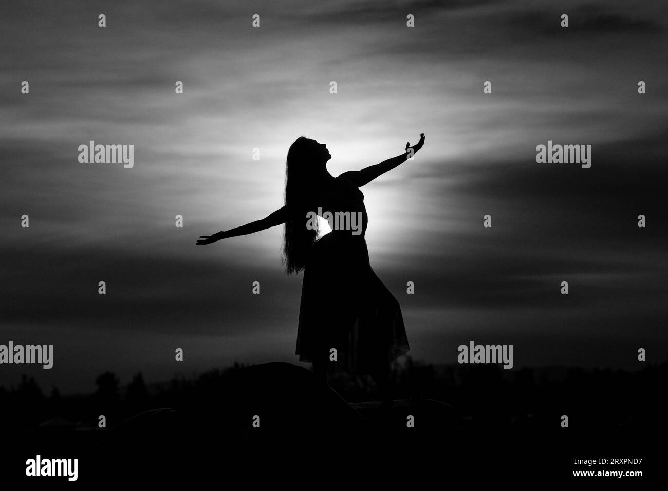 Silhouette di donna a pelo lungo in piedi contro il tramonto del sole Foto Stock