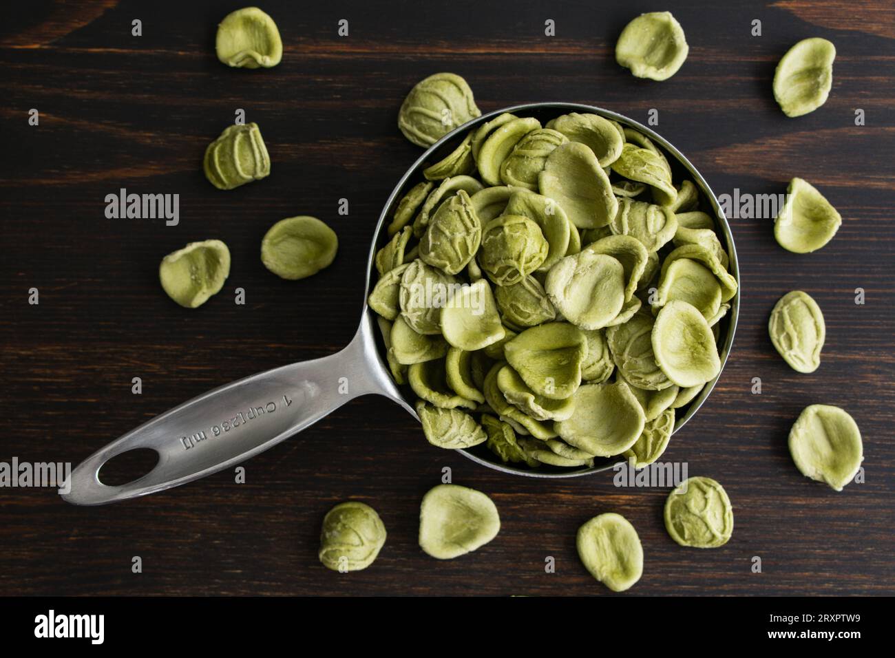 Orecchiette verdi essiccate in un dosatore: Orecchiette crude in un dosatore in metallo visto dall'alto Foto Stock